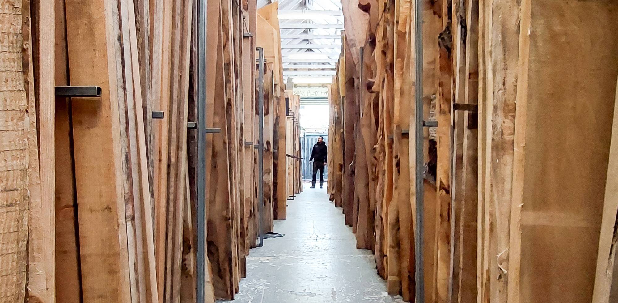 A timber yard with rows of boards stacked either side and a person in the distance